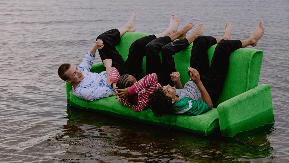 Friends sitting upside down on couch in river.